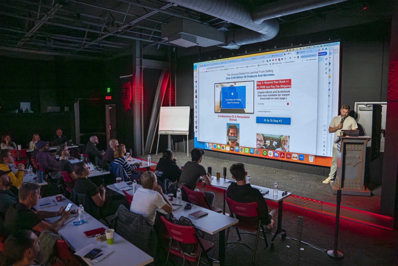 A packed room at the Pursuit of Profit Studio, presenter in front of the billboard screen